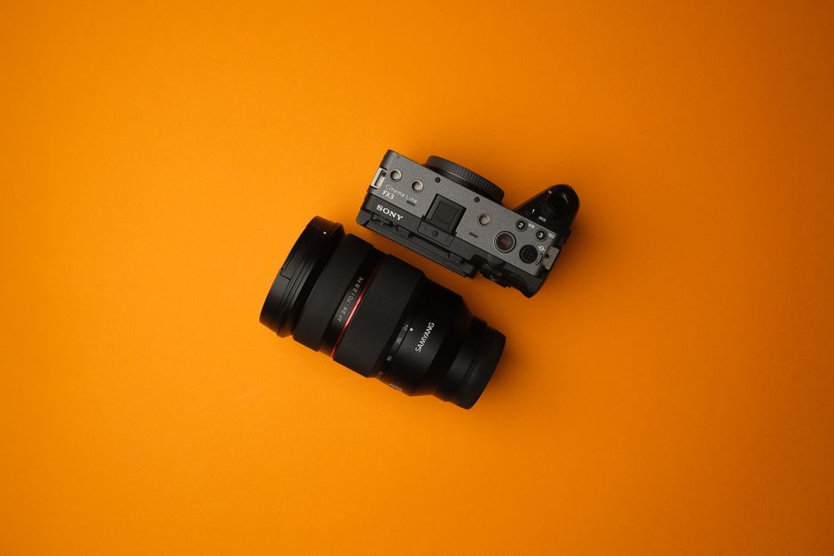 A professional camera with an attached lens on a vibrant orange background, showcasing modern photography technology.